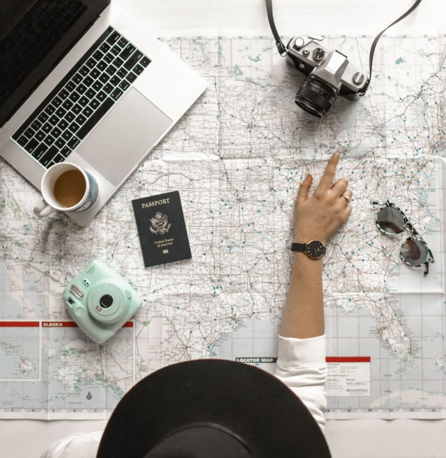 Hand pointing to a location on a map beside a laptop